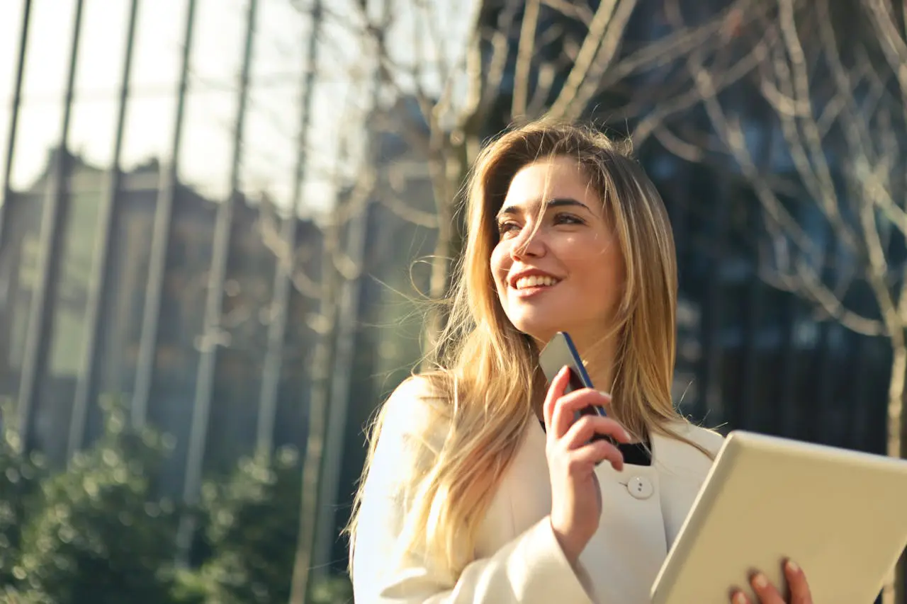 smiling businesswoman with phone and tablet outdoors